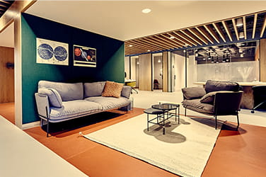 Lounge area with teal wall, grey sofas and rug and wooden flooring in a modern office fit out by ISG Ltd
