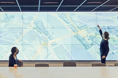 Two ISG employees in masks collaborating over a site map on a large screen behind a table