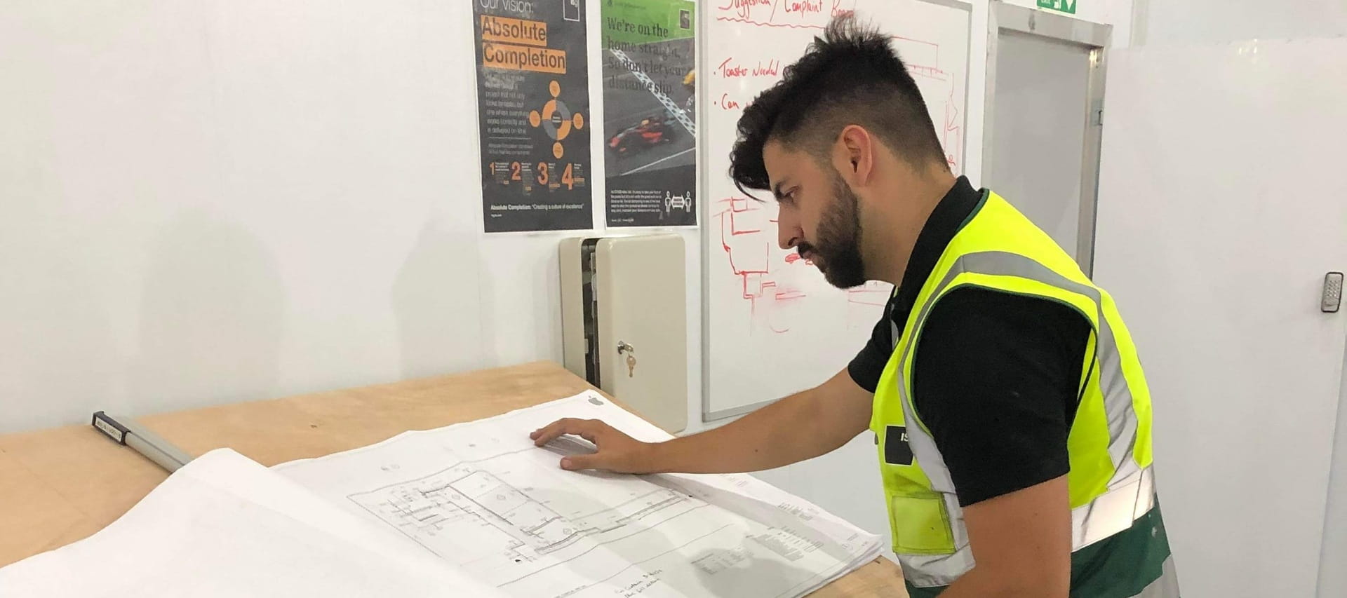 ISG Construction graduate Alex Riley in High vis looking at plans on table