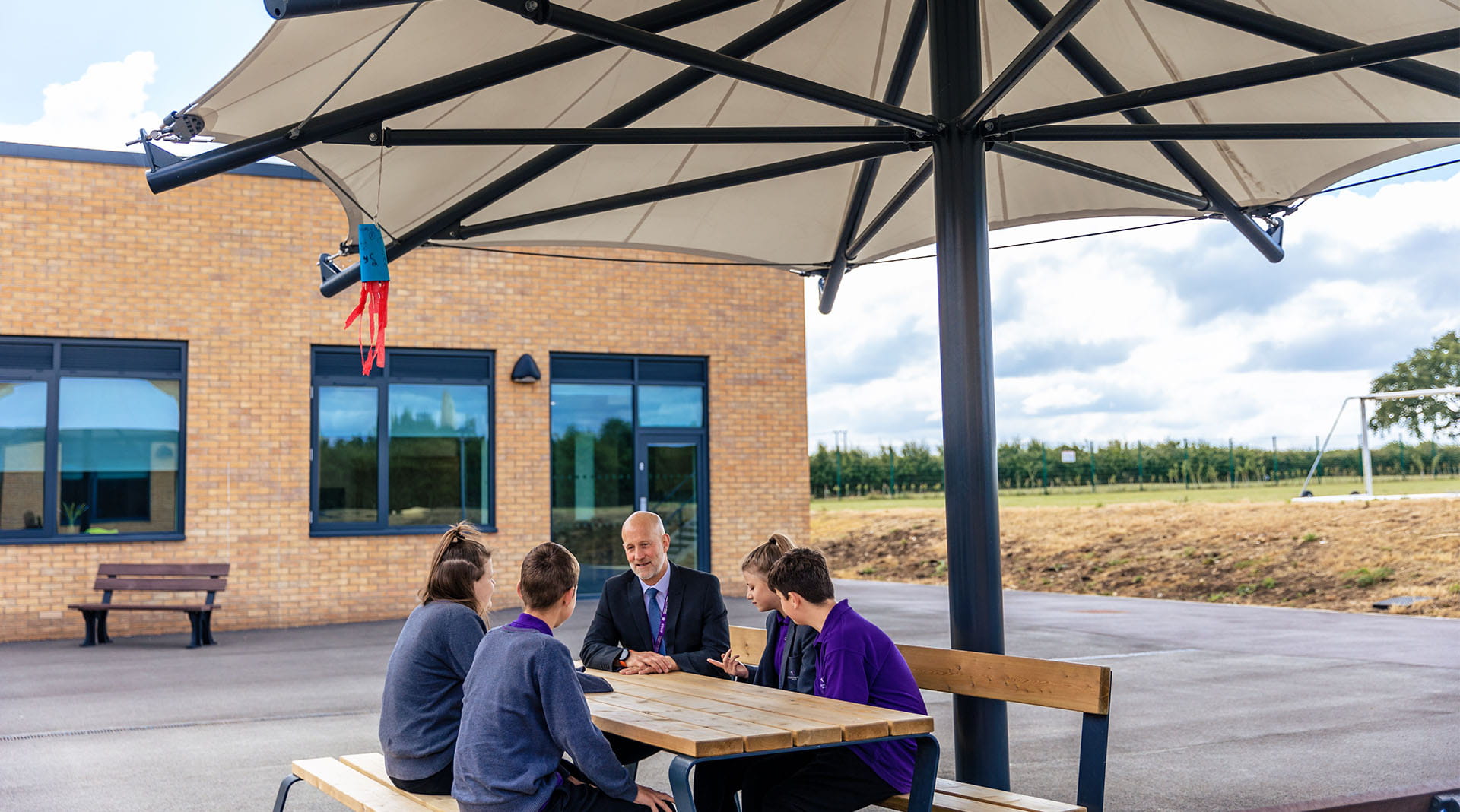 Headtreacher talking to students sat on a picnic bench in outdoor sheltered area area 