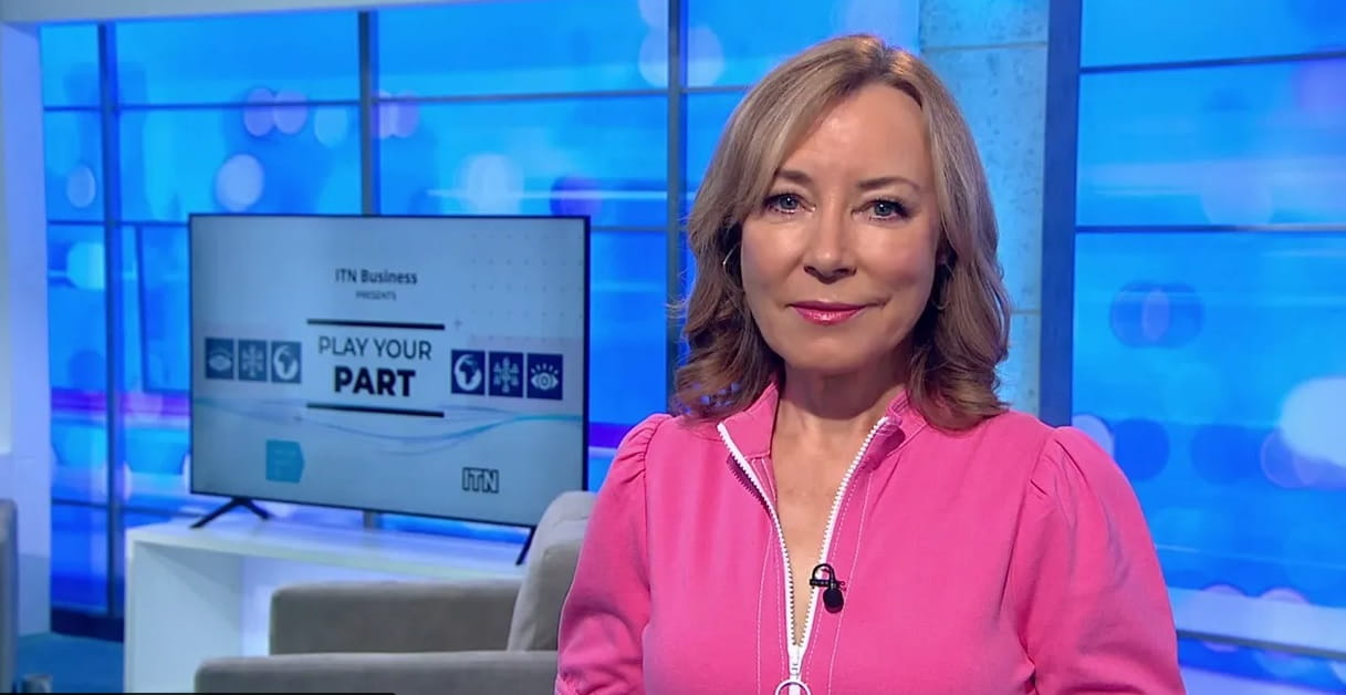 Photograph of a female news presenter in a pink top in a blue studio