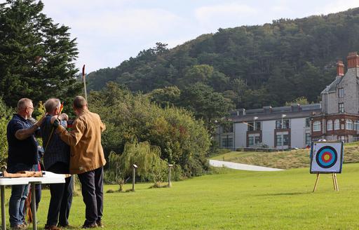 Mike and another instructor support one of the Blind Veterans. The arrow hurtles towards its target on the grass lawn.