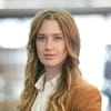 Headshot of ISG's head of sustainability for UK fit out and retail Anna Foden with long brown wavy hair wearing a white shirt and orange jacket