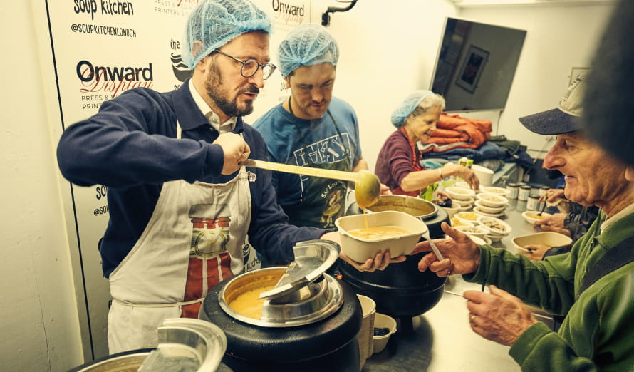 ISG staff ladelling soup into a dish at a soup kitchen