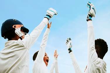 Three young cricketers with hands raised towards a blue sky